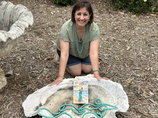 Tina kneeling beside the giant clam shell at the LA Arboretum with her book resting in it.