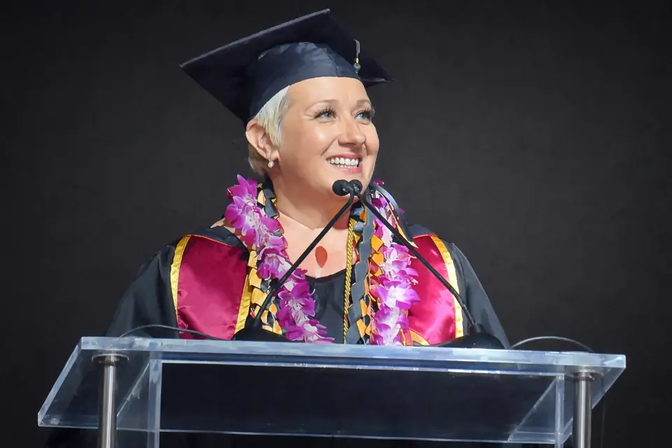 Tina Calderone-Roth speaking at a lectern in academic regalia.
